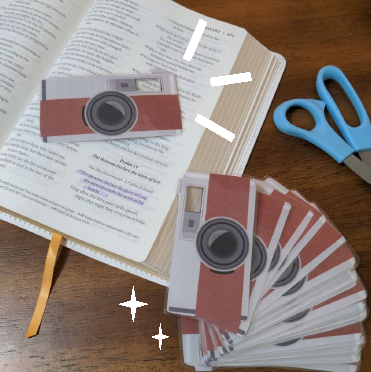 Paper camera print-outs near a Bible and scissors